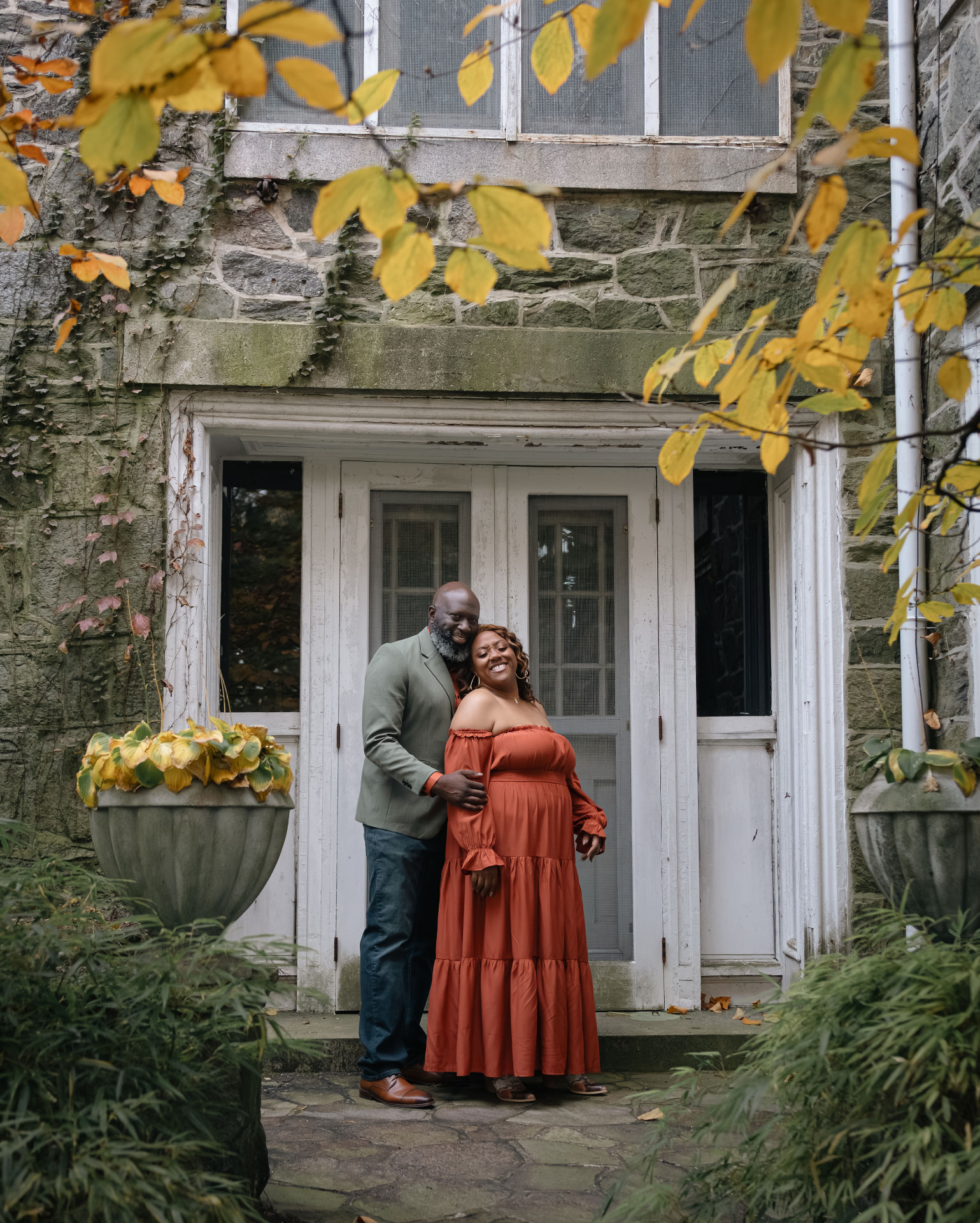 The couple embracing in a stone doorway beneath golden leaves